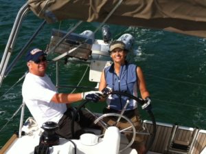Scott Rutherford in white shirt is sitting to left of his wife Sharon while she steers an Offshore Sailing School cruising boat