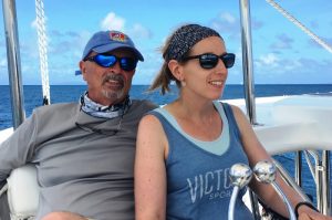 Close up of husband and wife sitting close together with wife steering in cockpit of a large sailing catamaran