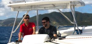 Chris Turner is learning to steer a big catamaran, with Offshore Sailing School instructor in red shirt, in the British Virgin Islands