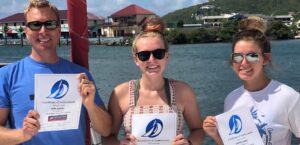 John Leuder and his two daughters Brigitte and Camille holding their Offshore Sailing School cruising course certificates on a boat in the BVI