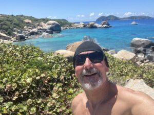 Offshore Sailing School graduate Thomas Rankin is taking a selfie of himself at The Baths in the BVI with catamaran in water behind him