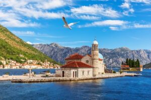 Tiny Church with gull flying above in water of harbor seen on flotilla cruise to Montenegro
