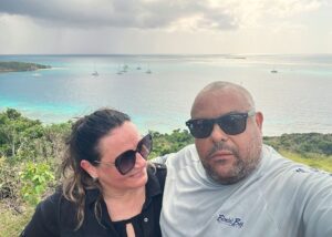 Woman and man taking selfie on hill with boats anchored in bay